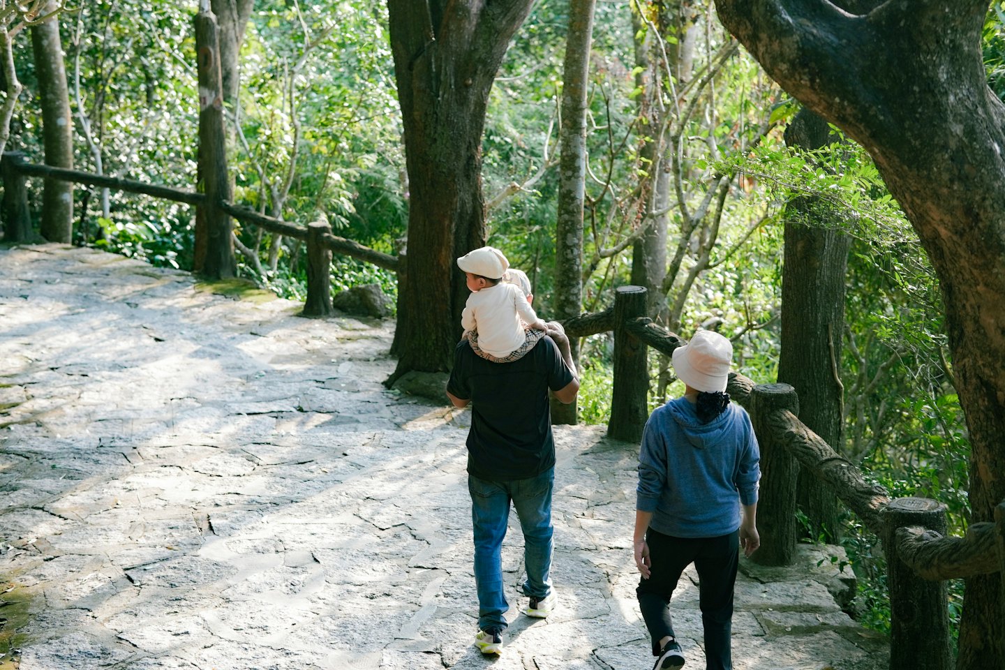 Famiglia passeggia su sentiero nel bosco con bimbo in spalla.